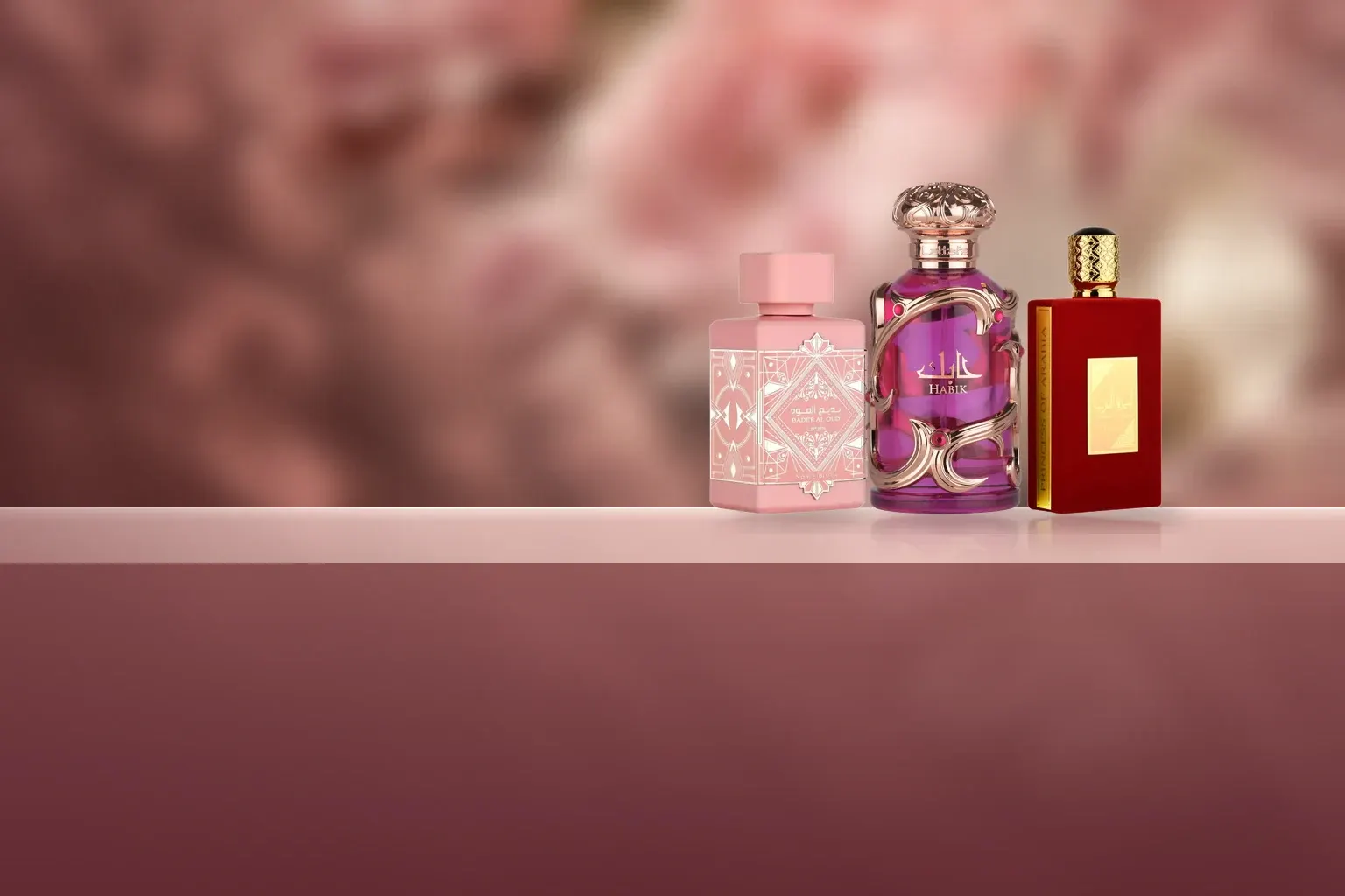 Lattafa Badee Al Oud Noble Blush, Habik for Women and Ameerat Al Arab bottles on a blush ledge in front of soft pink peonies